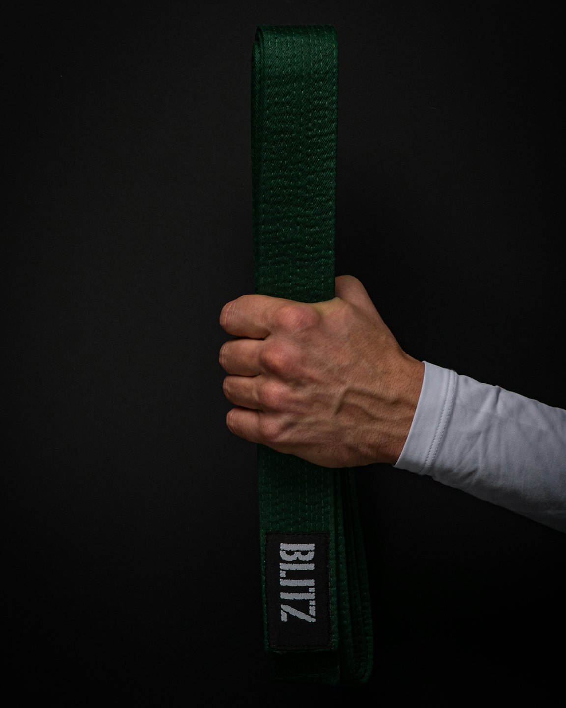Hand in uniform gripping a dark green martial arts belt.