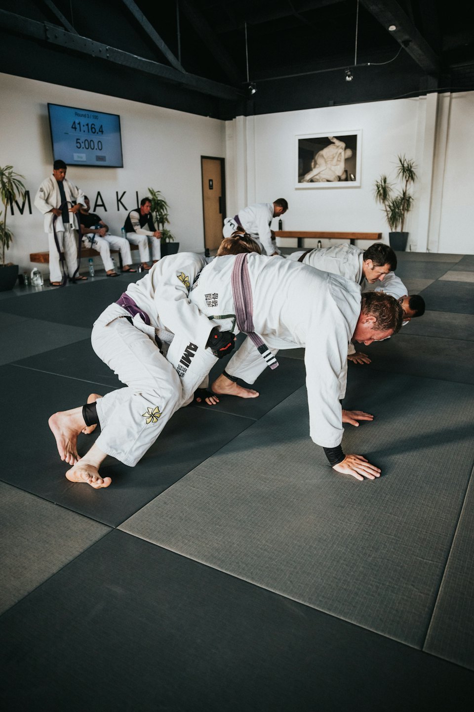 Men in white gis practice Brazilian Jiu-Jitsu push-ups on grey mats.