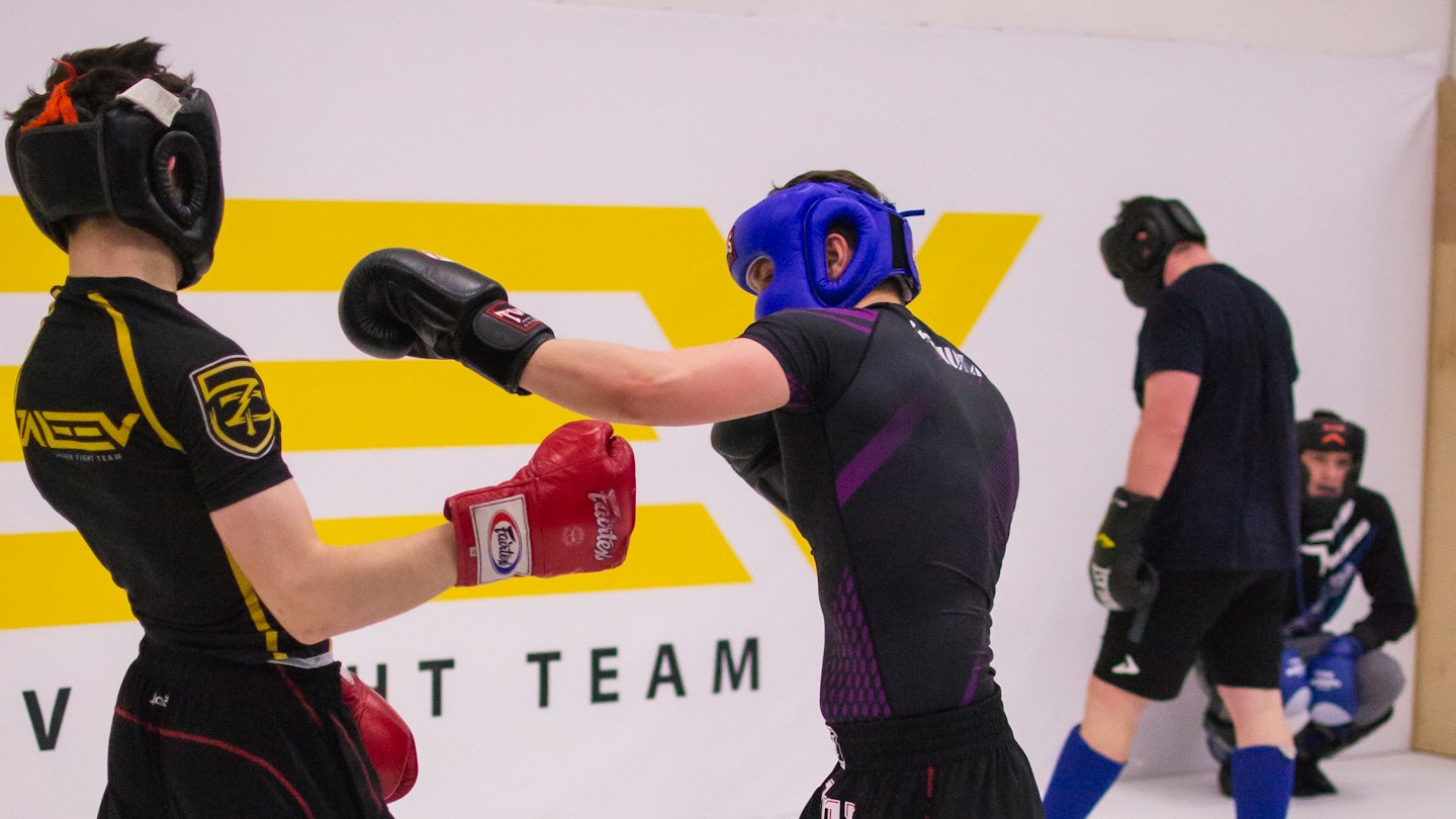 Four people practice martial arts sparring in a gym.